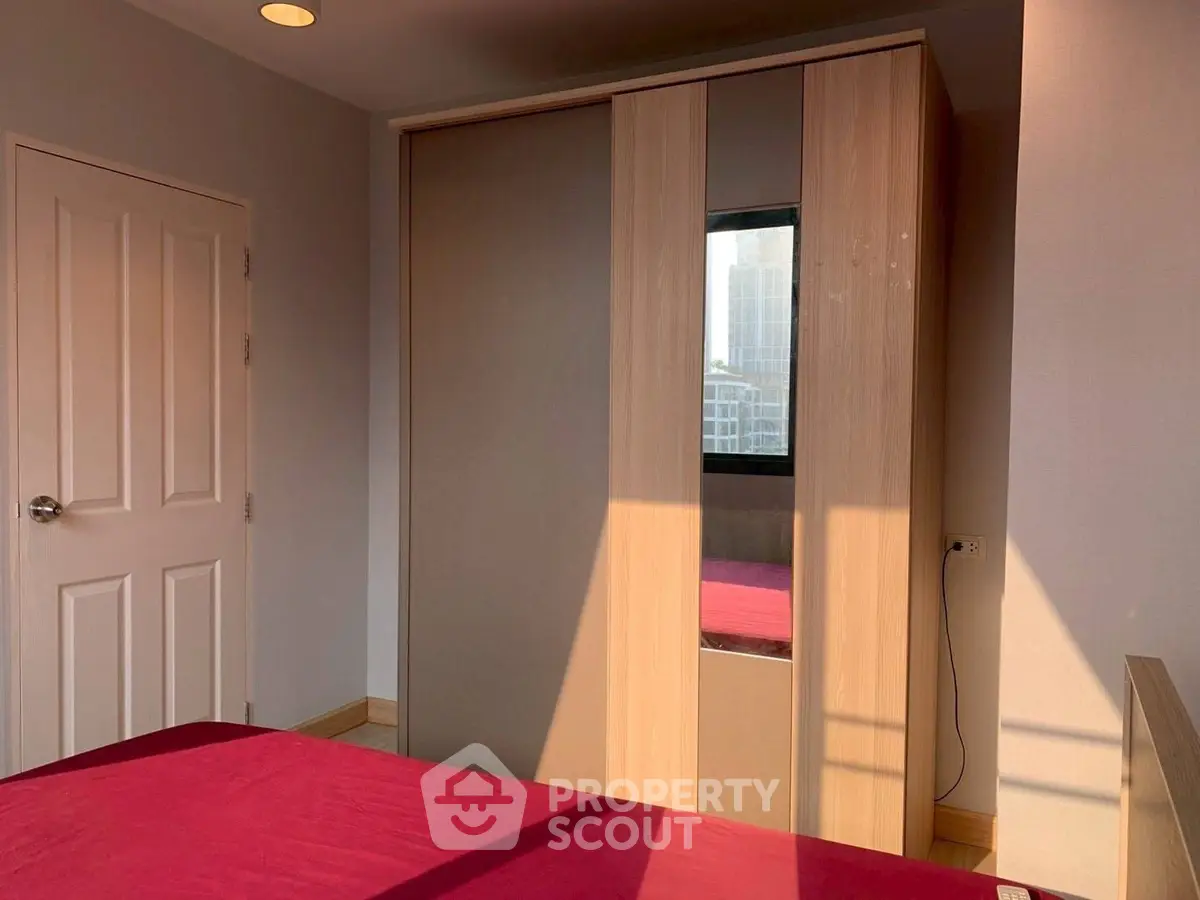 Cozy bedroom with modern wardrobe and city view window, perfect for urban living.