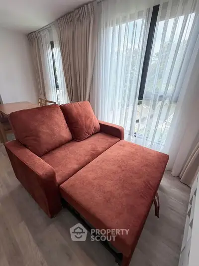 Spacious living room with stylish red sofa bed and large windows for natural light.