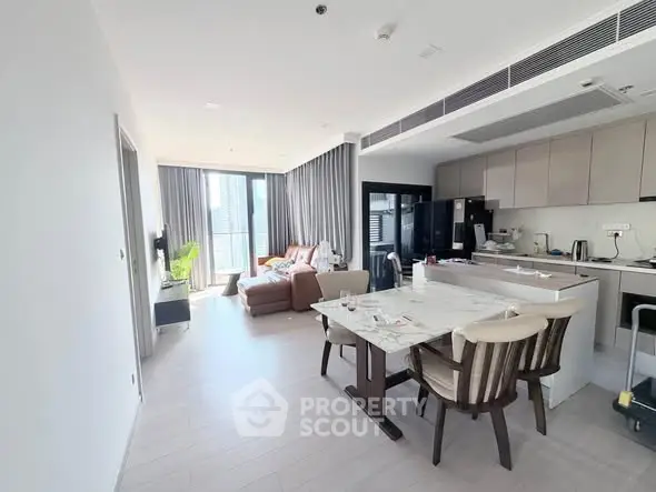 Modern open-layout living room and kitchen with natural light and stylish furnishings.