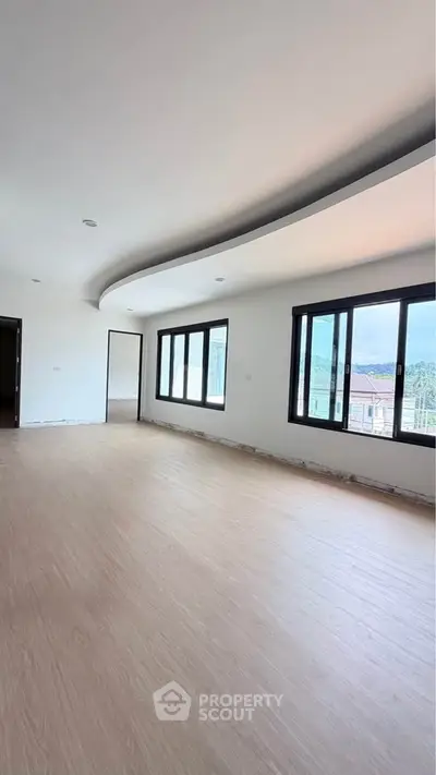 Spacious modern living room with large windows and elegant curved ceiling design.