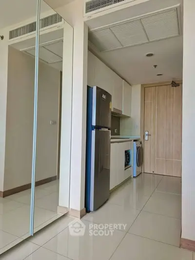 Modern apartment hallway with sleek kitchen appliances and mirrored closet doors.