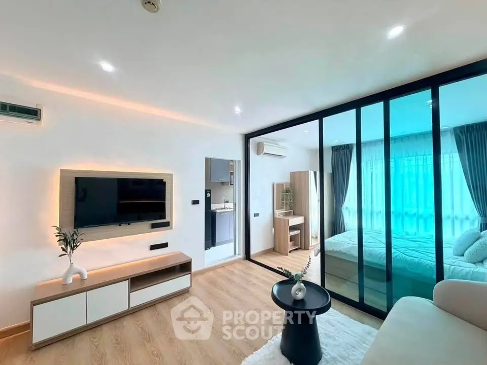 Modern living room with glass partition leading to a cozy bedroom, featuring sleek furniture and ambient lighting.