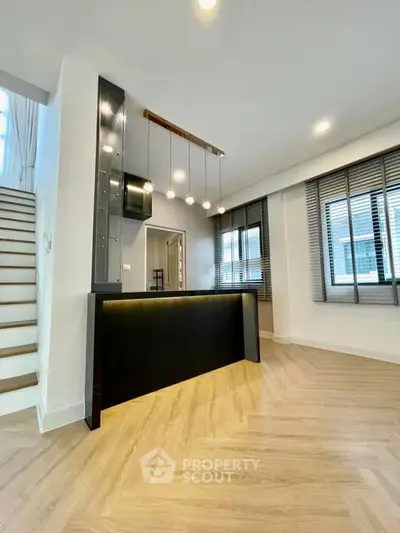 Modern interior with stylish lighting and wooden flooring, featuring a sleek staircase and large windows.