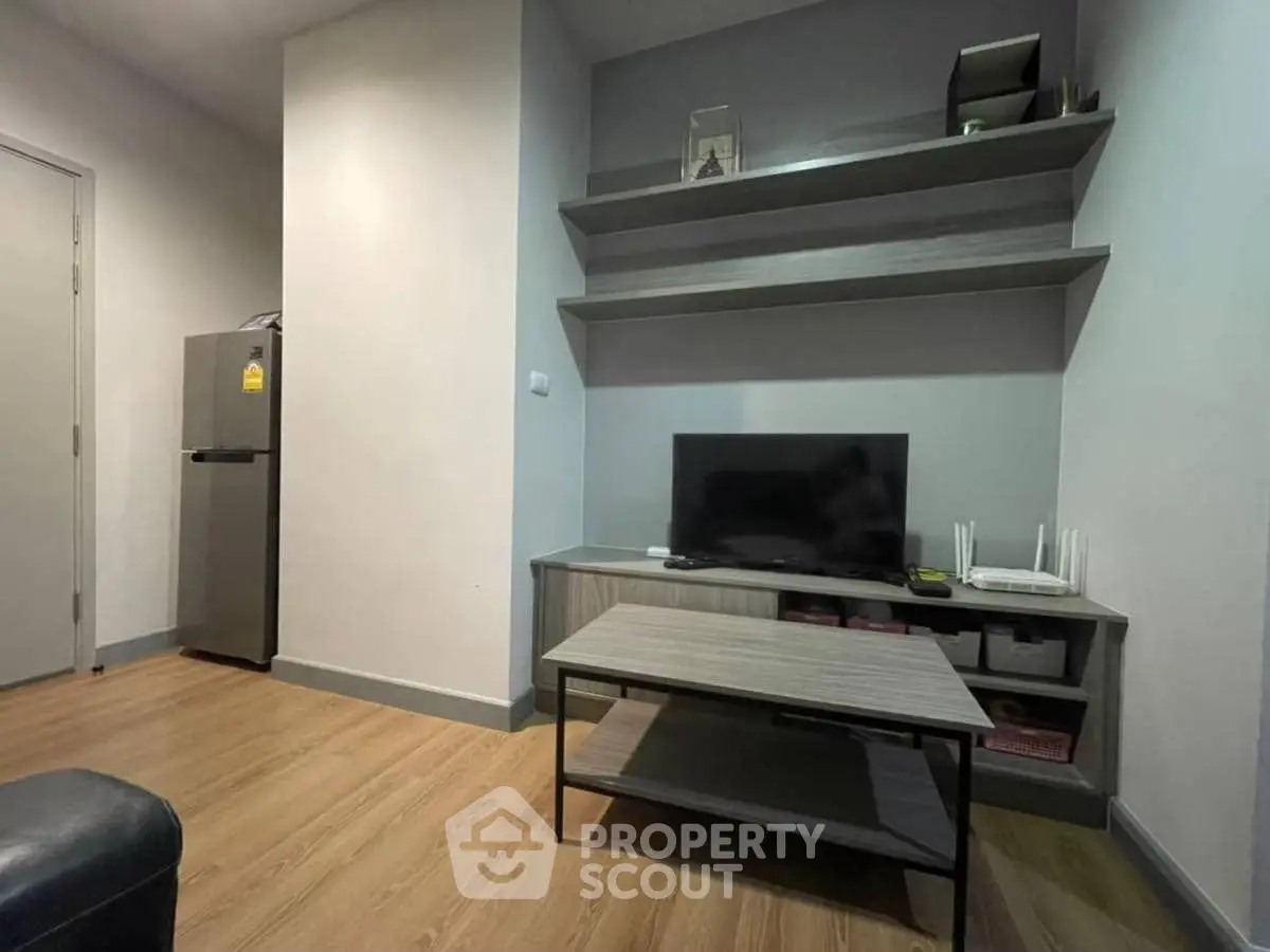 Modern living room with sleek TV stand and wooden flooring, featuring minimalist decor and a compact refrigerator.