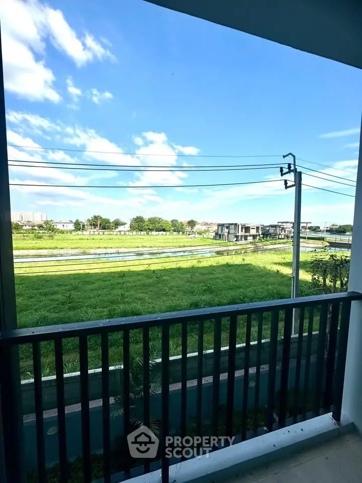 Charming balcony view overlooking lush green fields and distant modern homes.