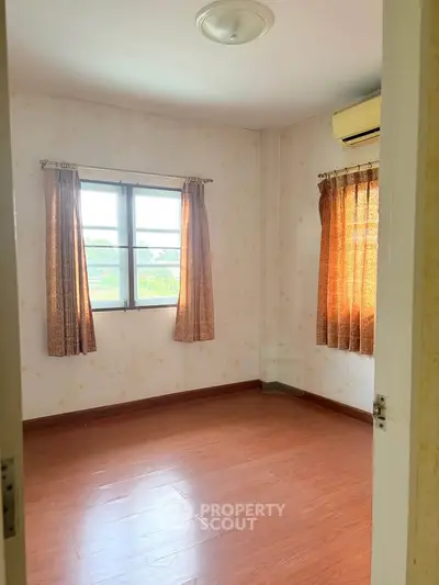 Bright empty bedroom with wooden flooring and large window, perfect for customization.