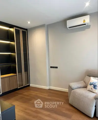 Modern living room with sleek built-in shelves and cozy armchair, featuring elegant wooden flooring and air conditioning.