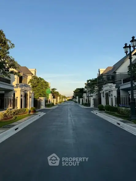 Charming suburban street with elegant houses and lush greenery under a clear blue sky.