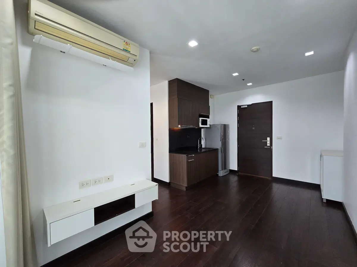 Modern apartment interior with dark wood flooring, compact kitchen, and air conditioning unit.