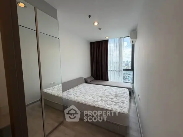 Modern bedroom with large window and city view, featuring a comfortable bed and mirrored wardrobe.
