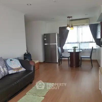 Cozy living room with dining area and modern fridge, wooden flooring, and natural light.