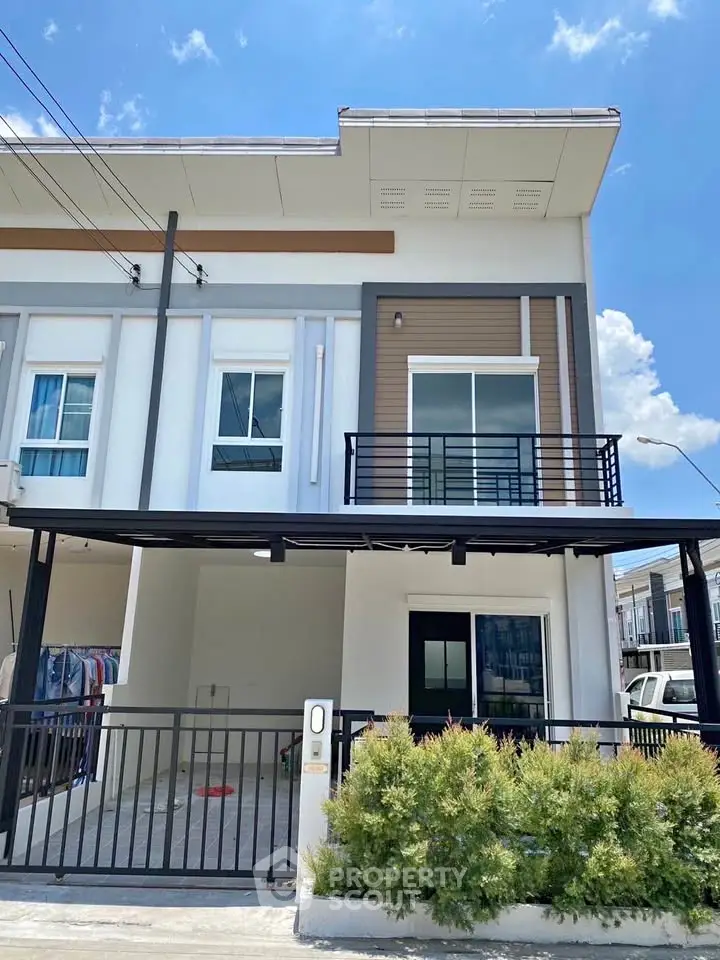 Modern townhouse exterior with balcony and gated entrance under clear blue sky.