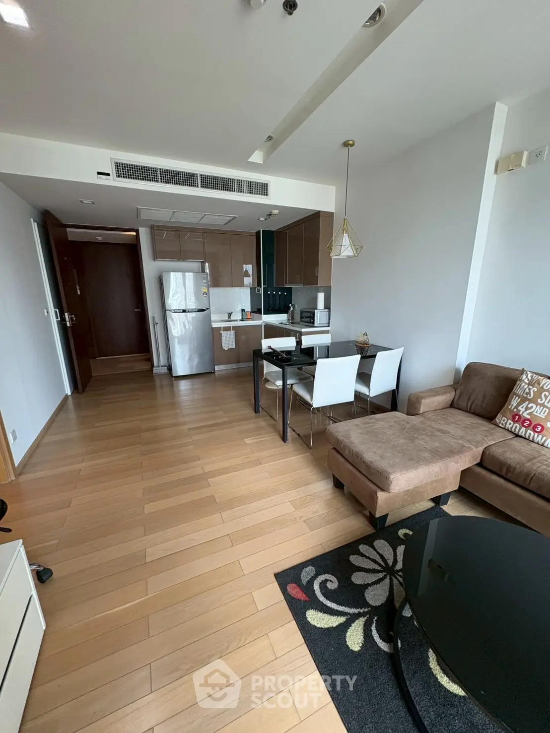 Modern open-layout living room with kitchen and dining area, featuring stylish furniture and wooden flooring.