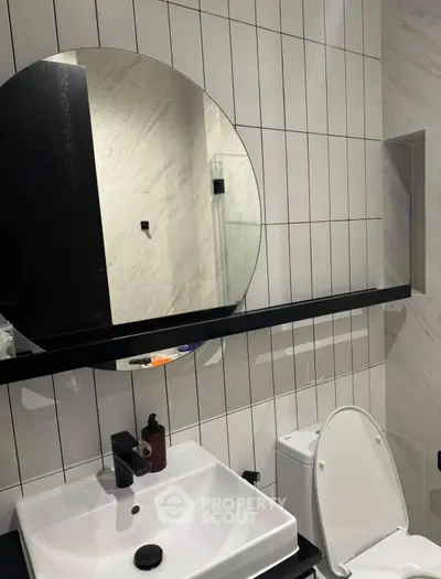 Modern bathroom with sleek design featuring round mirror and stylish fixtures.