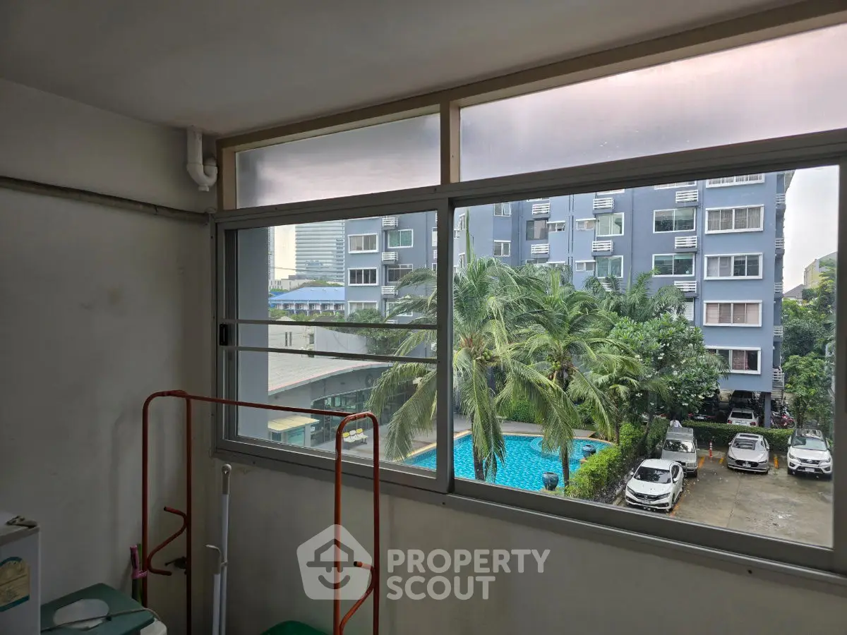 Apartment window view overlooking pool and parking area with palm trees.