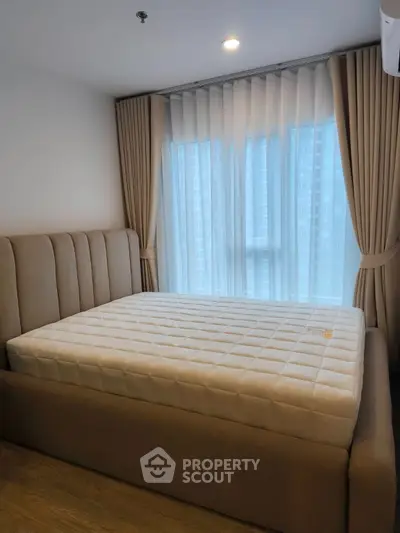 Cozy bedroom with plush bed and floor-to-ceiling window offering natural light.