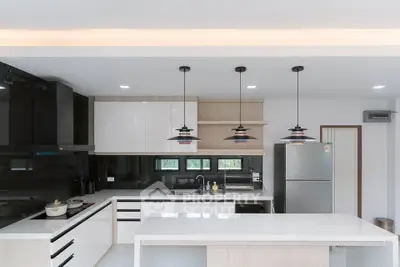 Modern kitchen with sleek design, featuring island, pendant lights, and stainless steel appliances.