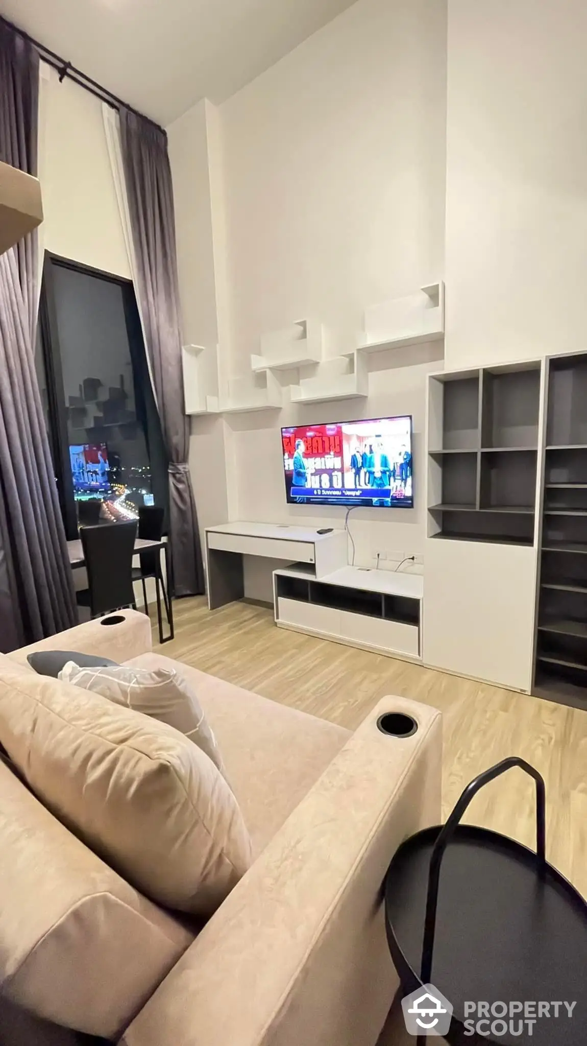 Cozy modern living room with plush sofa, sleek entertainment unit, and floor-to-ceiling window offering a cityscape view, perfect for urban living.