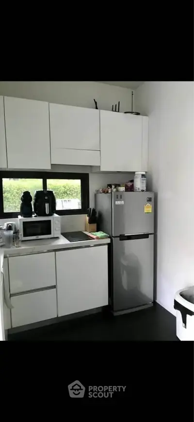 Modern compact kitchen with sleek white cabinets and stainless steel fridge, perfect for urban living.
