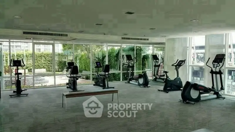 Spacious gym with modern exercise equipment and large windows offering garden views.