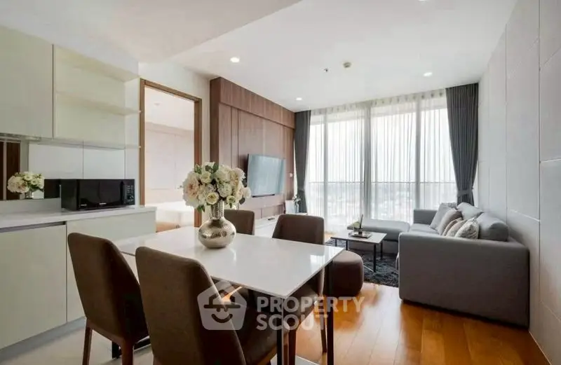 Modern living room with open kitchen, stylish decor, and large windows offering natural light.