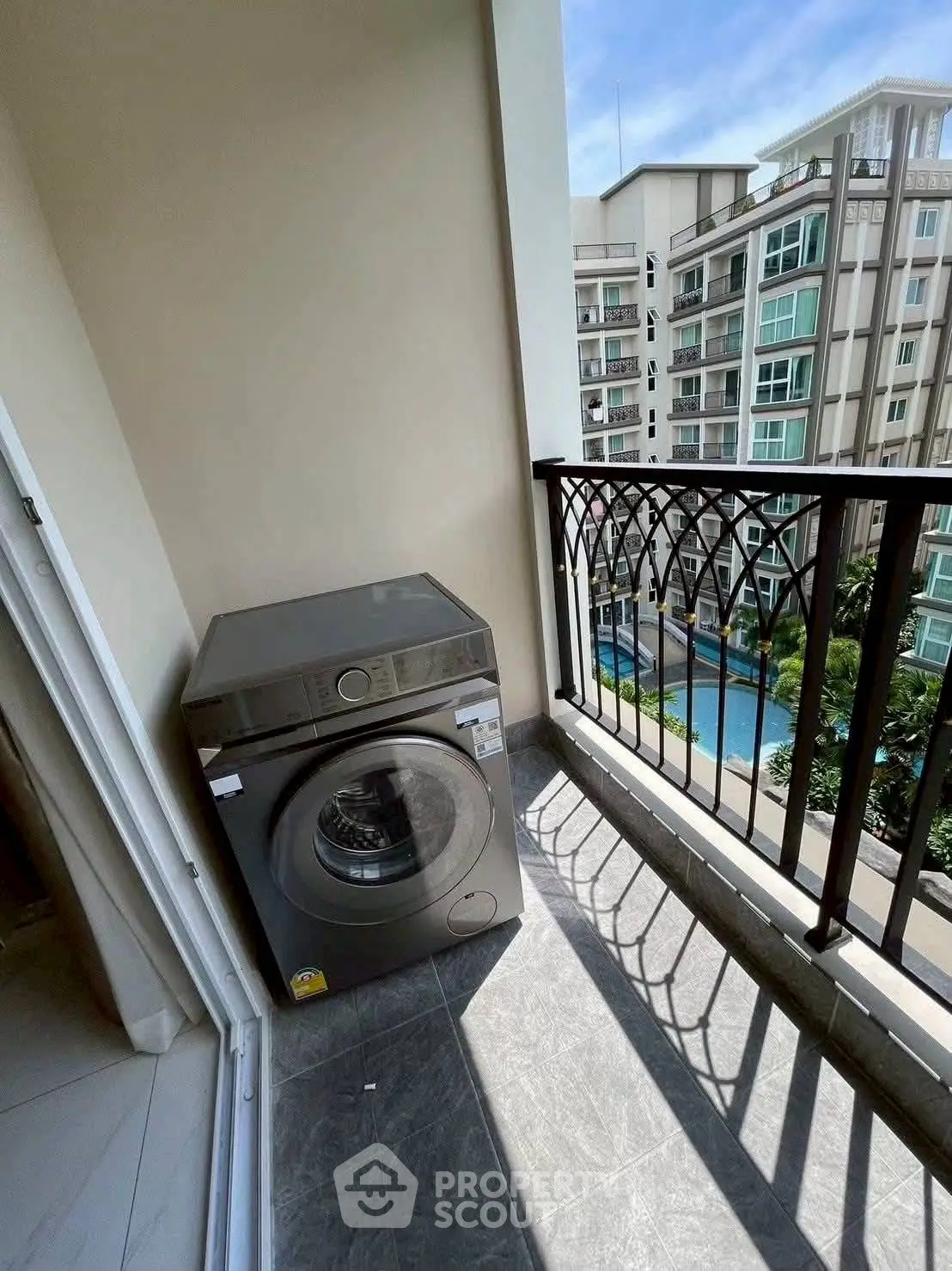 Modern balcony with washing machine overlooking pool and residential buildings.