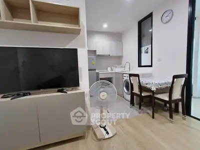 Modern living area with TV, fan, and compact kitchen in open layout apartment.