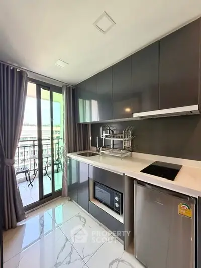 Modern kitchen with sleek cabinets and balcony view, featuring compact appliances and elegant design.