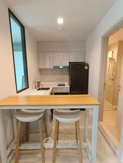 Modern compact kitchen with breakfast bar and adjacent bathroom in a stylish apartment.