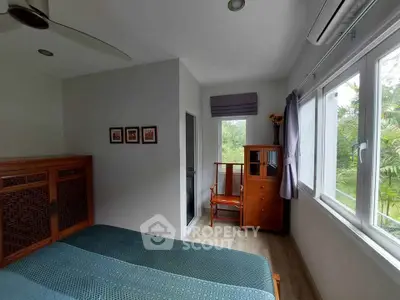 Cozy bedroom with large windows and wooden furniture, offering a serene garden view.