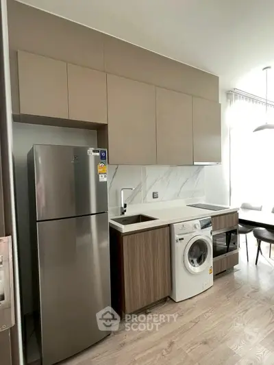 Modern kitchen with sleek cabinets, stainless steel fridge, and washing machine in a stylish apartment.