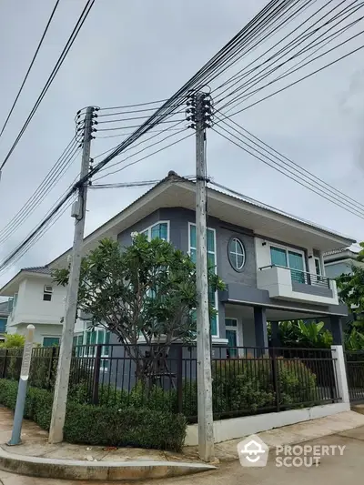 Modern two-story house with lush greenery and secure fencing in a suburban neighborhood.