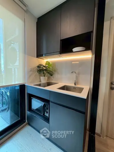 Modern compact kitchen with sleek black cabinets and built-in appliances, featuring a large window for natural light.