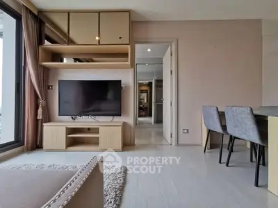 Modern living room with large TV and dining area, featuring sleek furniture and natural light.