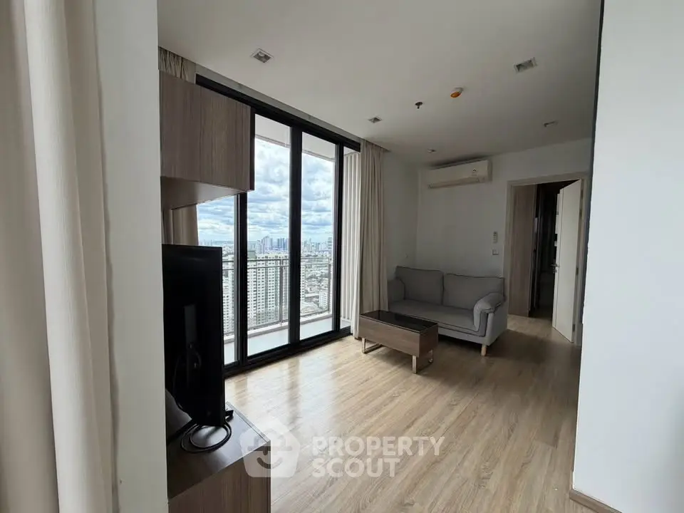 Modern living room with large windows offering stunning city views, featuring sleek furniture and wooden flooring.