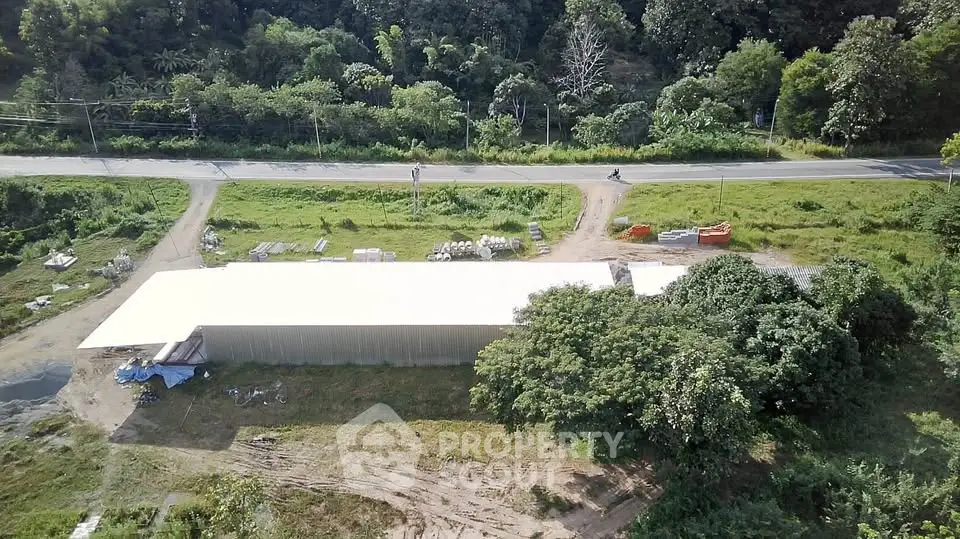 Aerial view of a large warehouse surrounded by lush greenery and a nearby road.