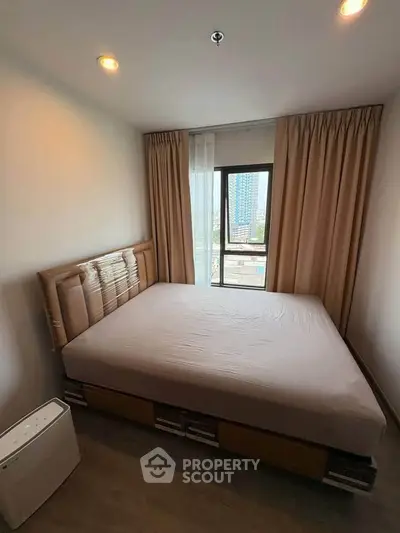 Cozy bedroom with large window offering city view, featuring modern bed and neutral decor.