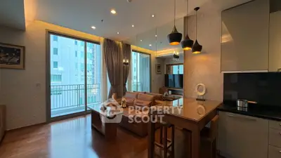 Modern living room with open kitchen and balcony view, featuring stylish lighting and cozy seating area.