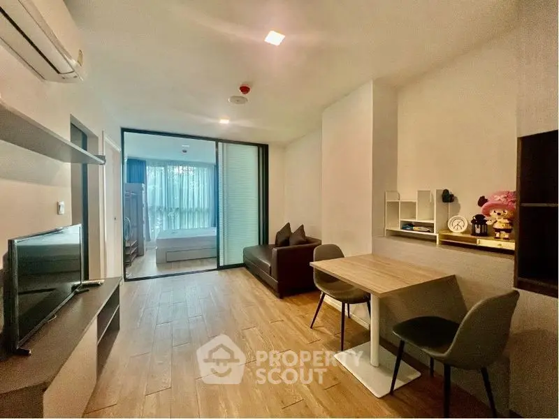 Modern living room with dining area and view into bedroom, featuring sleek furniture and wooden flooring.