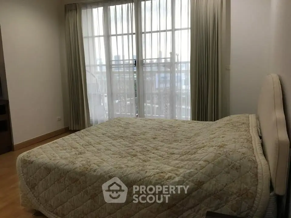 Cozy bedroom with large window and elegant curtains, featuring a comfortable bed and wooden flooring.