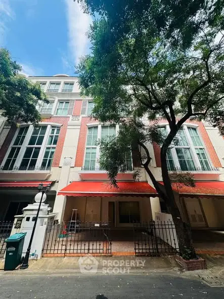 Charming multi-story building with red awnings and lush trees in a serene neighborhood.