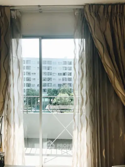 Bright apartment view with balcony overlooking modern building and lush greenery.