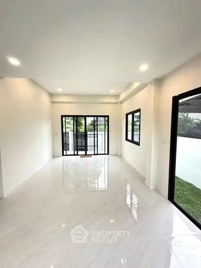 Spacious modern living room with large windows and glossy tiled floor, offering abundant natural light.