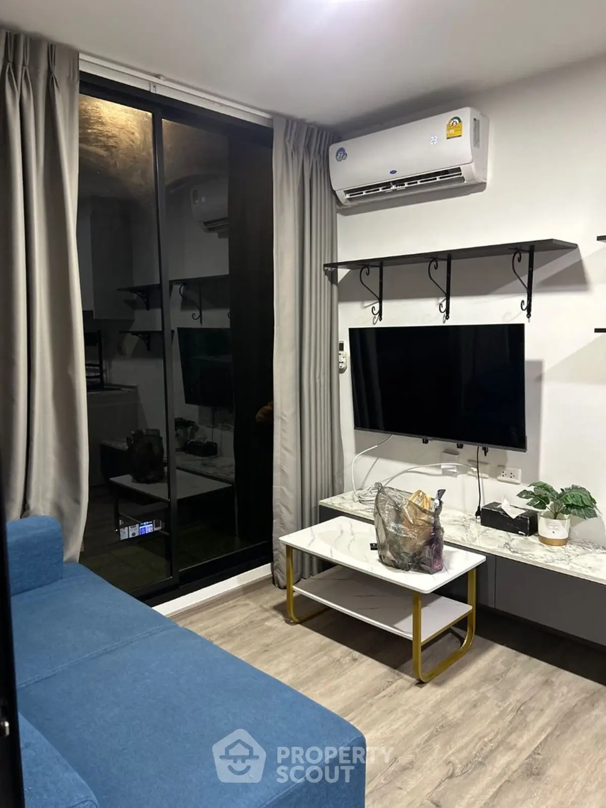 Modern living room with blue sofa, wall-mounted TV, and air conditioning