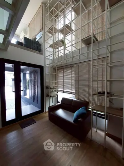 Modern loft-style living room with high ceilings and large windows, featuring a cozy sofa and stylish shelving.