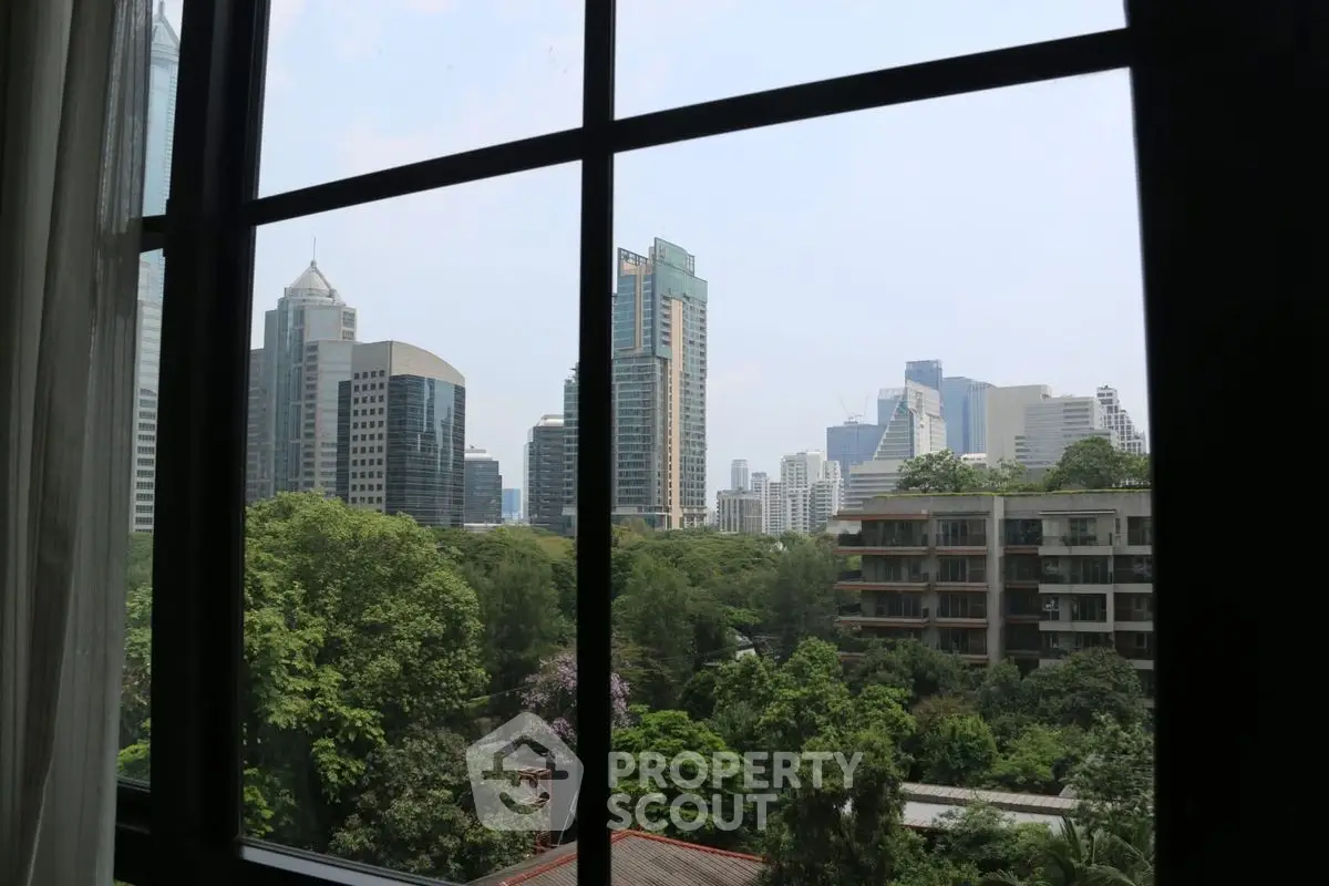 Stunning cityscape view from a window overlooking lush greenery and modern skyscrapers.