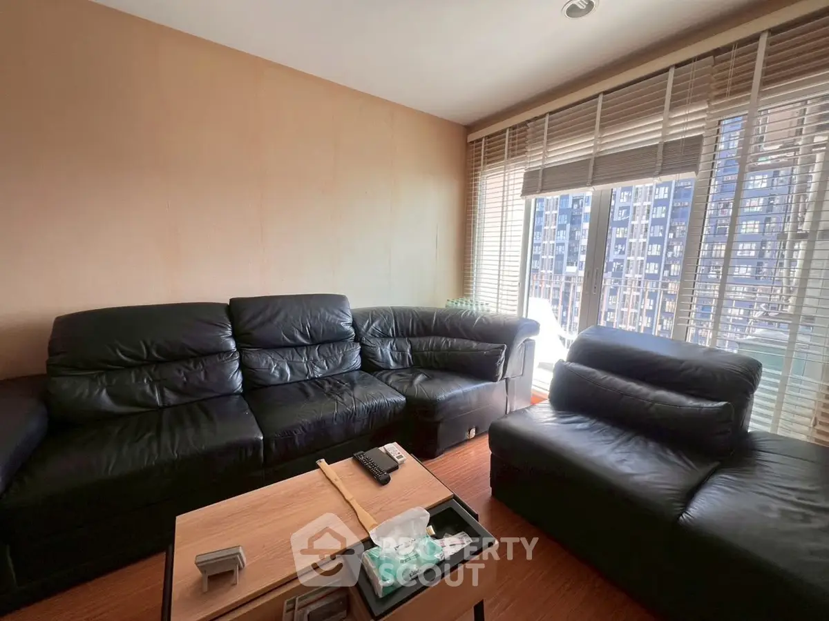 Spacious living room with black leather sofas and large windows offering city views.