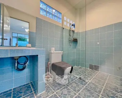 Spacious bathroom with modern blue tile design and glass shower enclosure.
