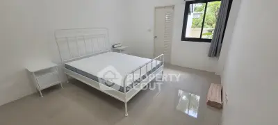 Minimalist bedroom with white metal bed frame and large window offering natural light.