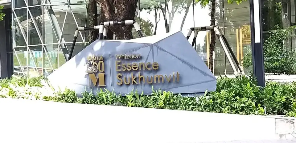Modern building entrance with sleek signage and lush greenery at Essence Sukhumvit.